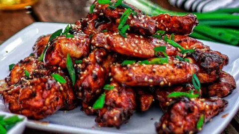 Plate of spicy grilled chicken wings garnished with sesame seeds and green onions on a wooden table.