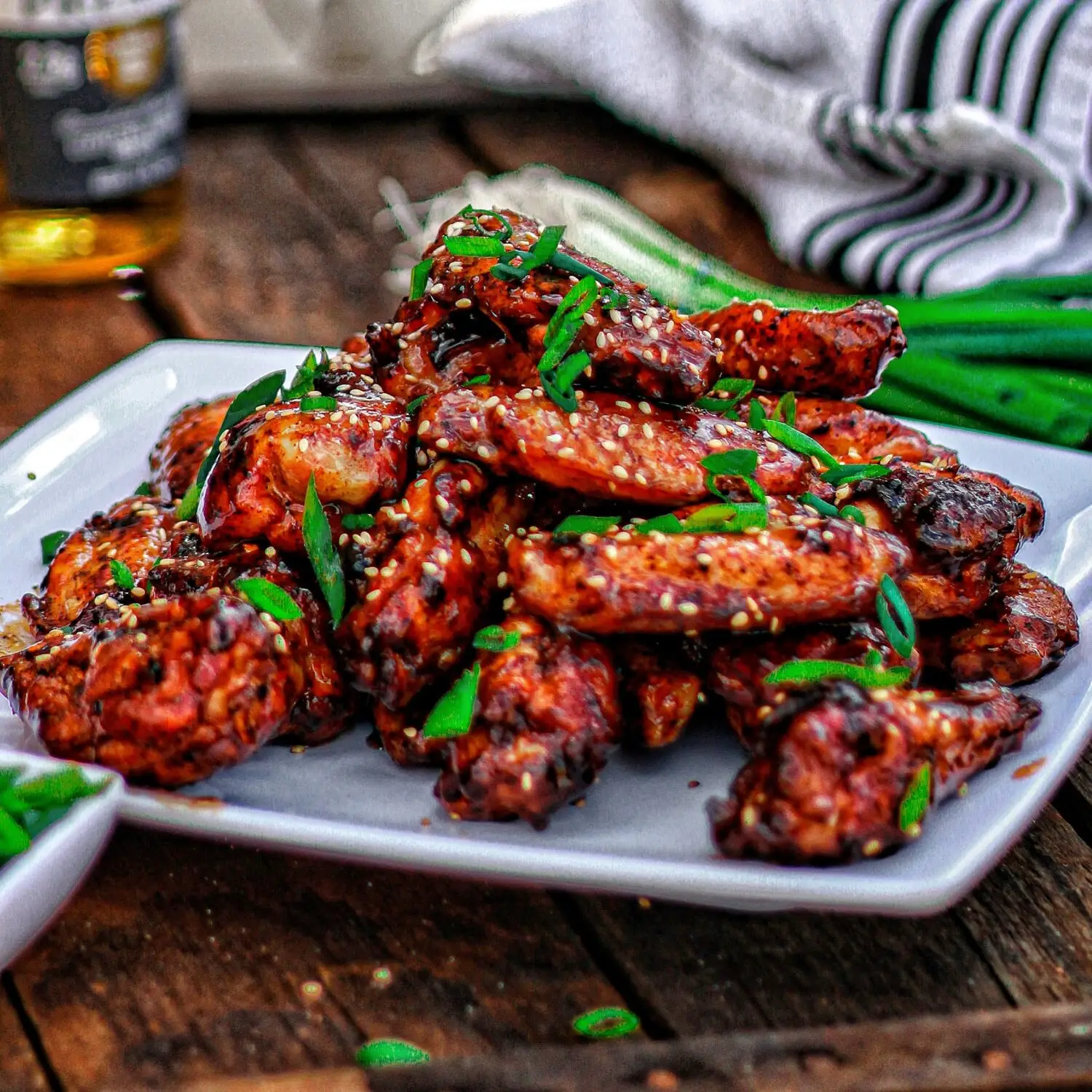 Plate of spicy grilled chicken wings garnished with sesame seeds and green onions on a wooden table.