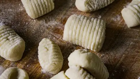 Homemade gnocchi on a wooden board dusted with flour, ready for cooking. Rustic Italian culinary preparation.