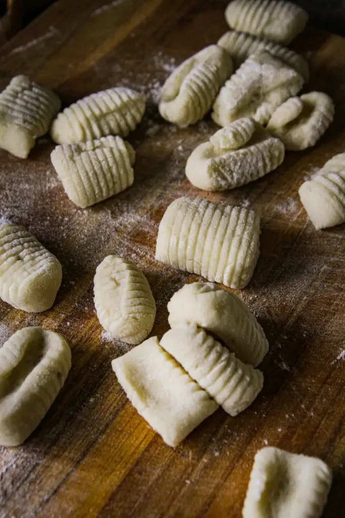 Homemade gnocchi on a wooden board dusted with flour, ready for cooking. Rustic Italian culinary preparation.