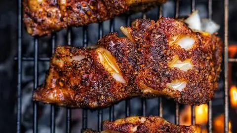 Grilled spiced fish filets on a barbecue grill with flames in the background, showcasing a crispy, seasoned crust.