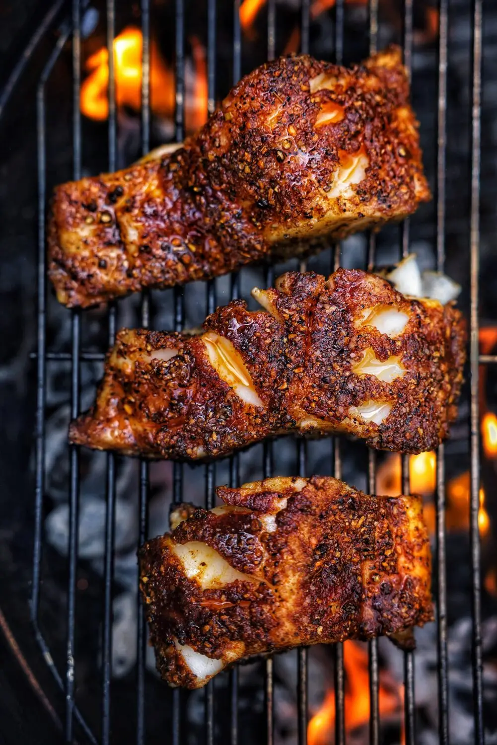 Grilled spiced fish filets on a barbecue grill with flames in the background, showcasing a crispy, seasoned crust.