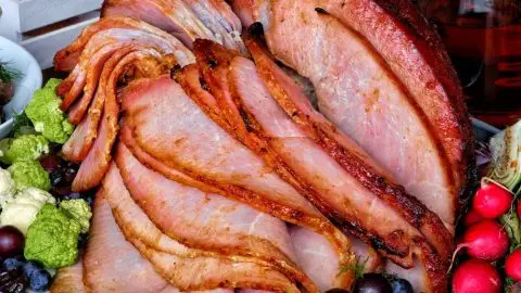 Sliced glazed ham with fresh fruits and veggies on a tray, ideal for festive gatherings and holiday meals.