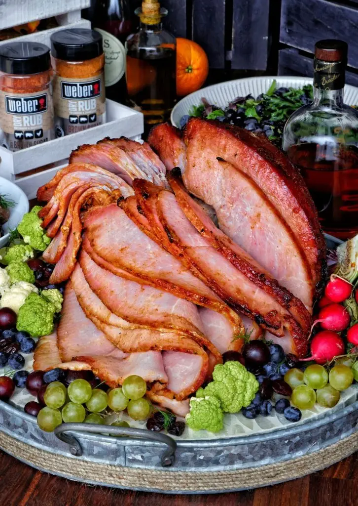 Sliced glazed ham with fresh fruits and veggies on a tray, ideal for festive gatherings and holiday meals.