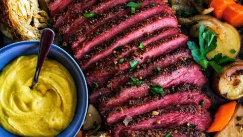 Sliced corned beef with roasted vegetables and mustard dip on a tray. Perfect for a savory dinner.