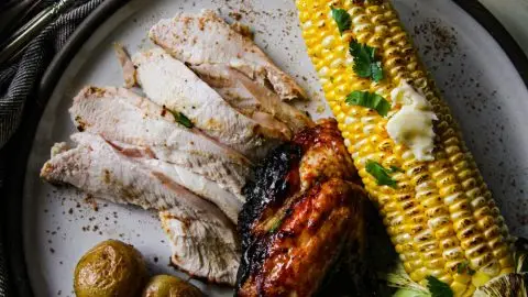 Grilled chicken with roasted potatoes, corn on the cob, and a glass of white wine on a plate with parsley garnish.