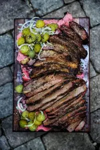 Sliced grilled brisket with pickles and onions on a wooden board, perfect for a delicious barbecue meal.