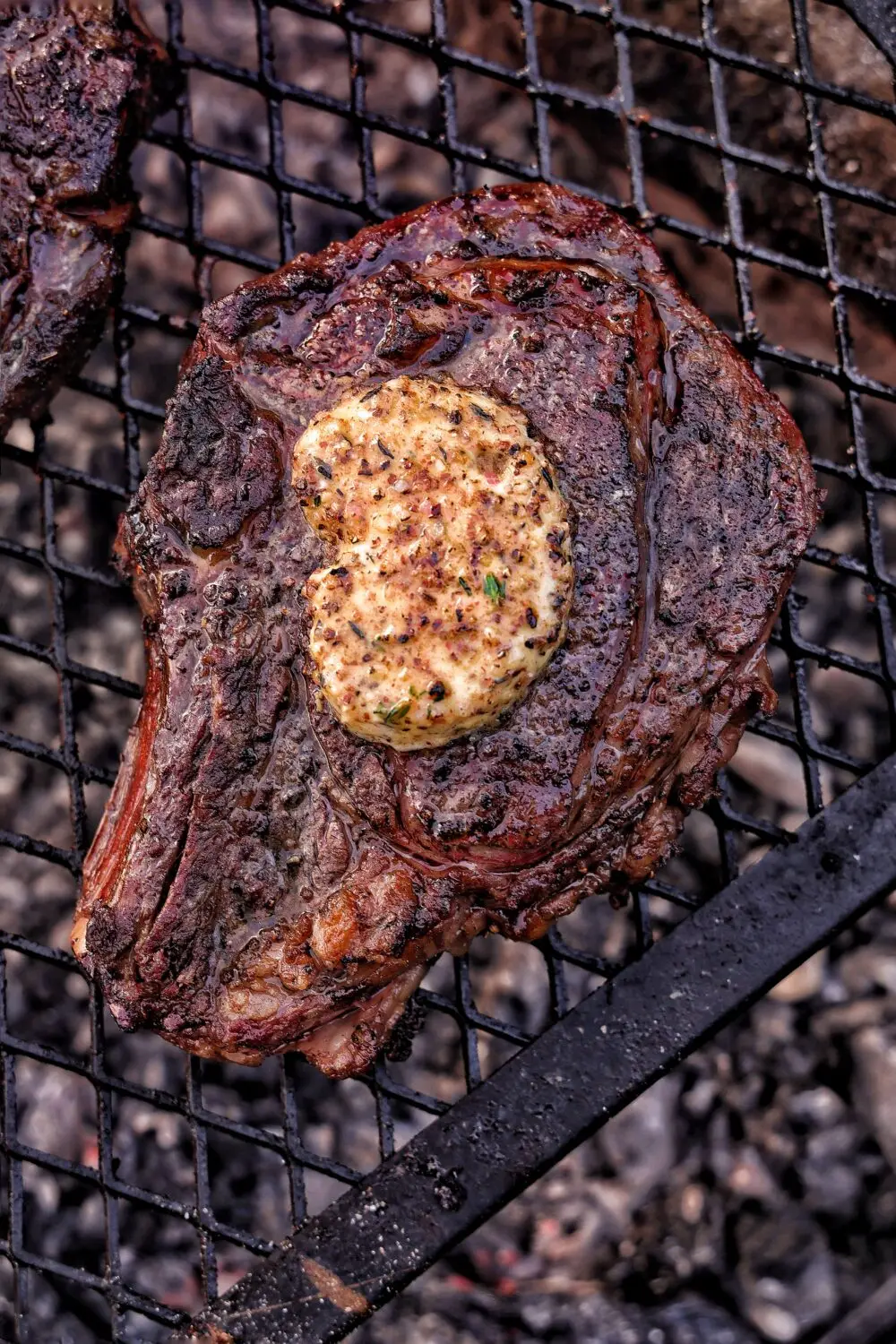 Grilled steak with herb butter melting on top on a barbecue grill, close-up shot.