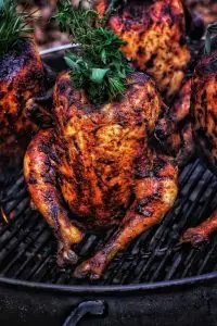 Whole grilled chicken with herbs, perfectly roasted on a barbecue grill, showcasing crispy skin and savory flavor.