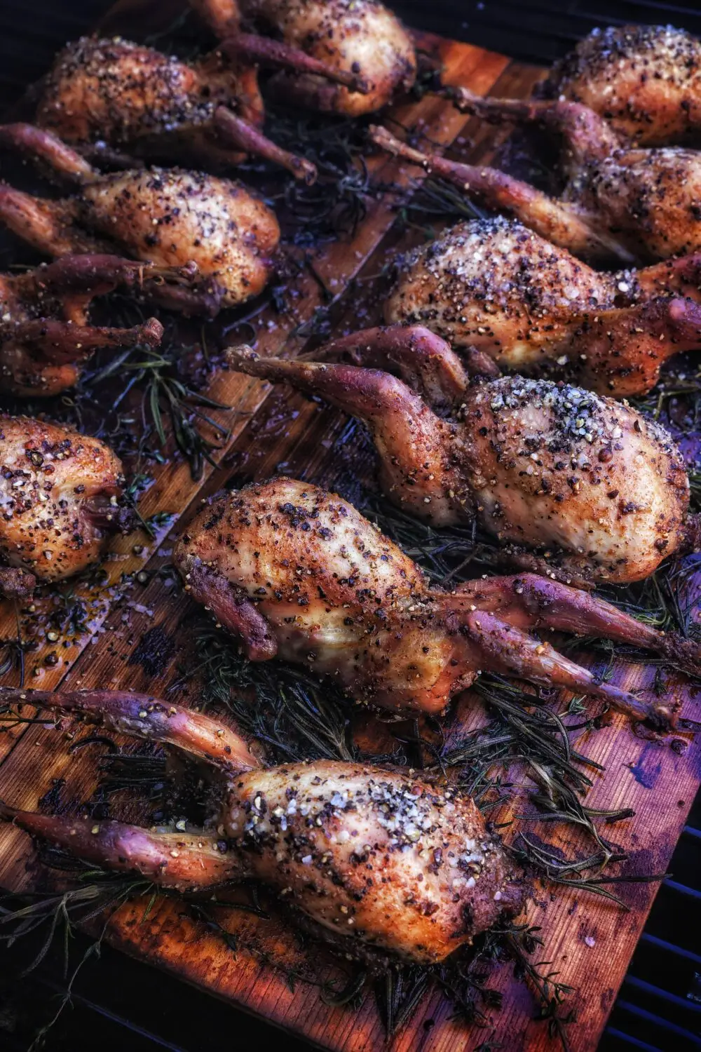 Grilled quails seasoned with pepper and herbs on a wooden plank for a delicious outdoor barbecue feast.