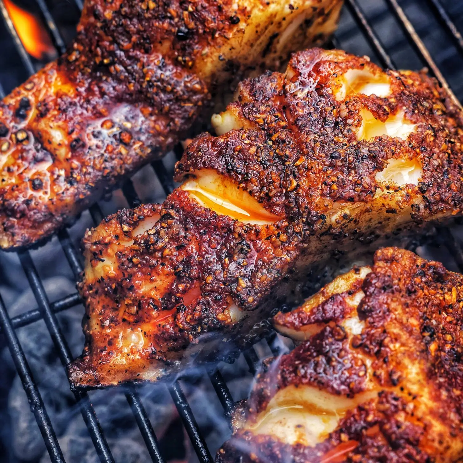Close-up of juicy grilled chicken with a crispy, spicy coating on a barbecue grill.