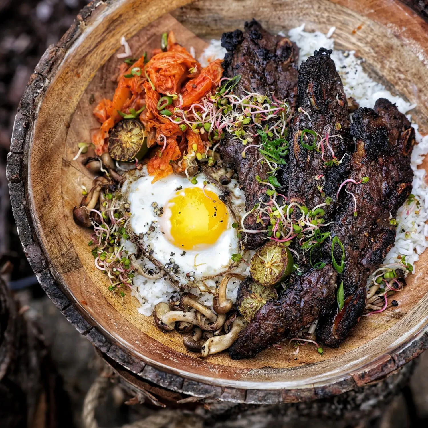Bowl of grilled beef, fried egg, kimchi, rice, mushrooms, and sprouts in a wooden bowl, perfect Asian fusion meal.