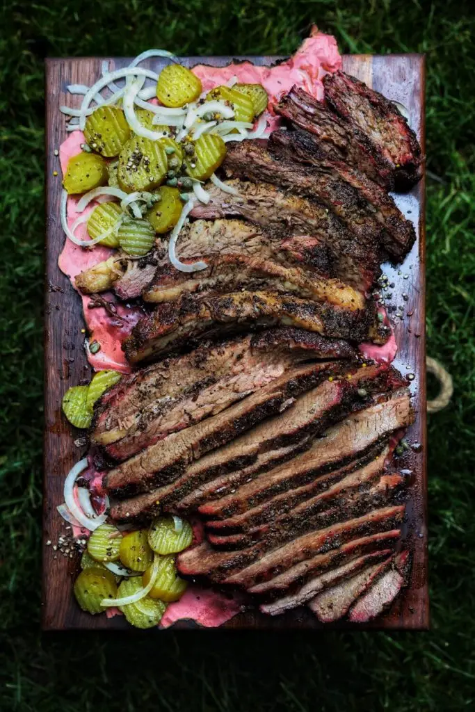 Sliced smoked brisket served with pickles and onions on a wooden board, perfect for BBQ lovers.