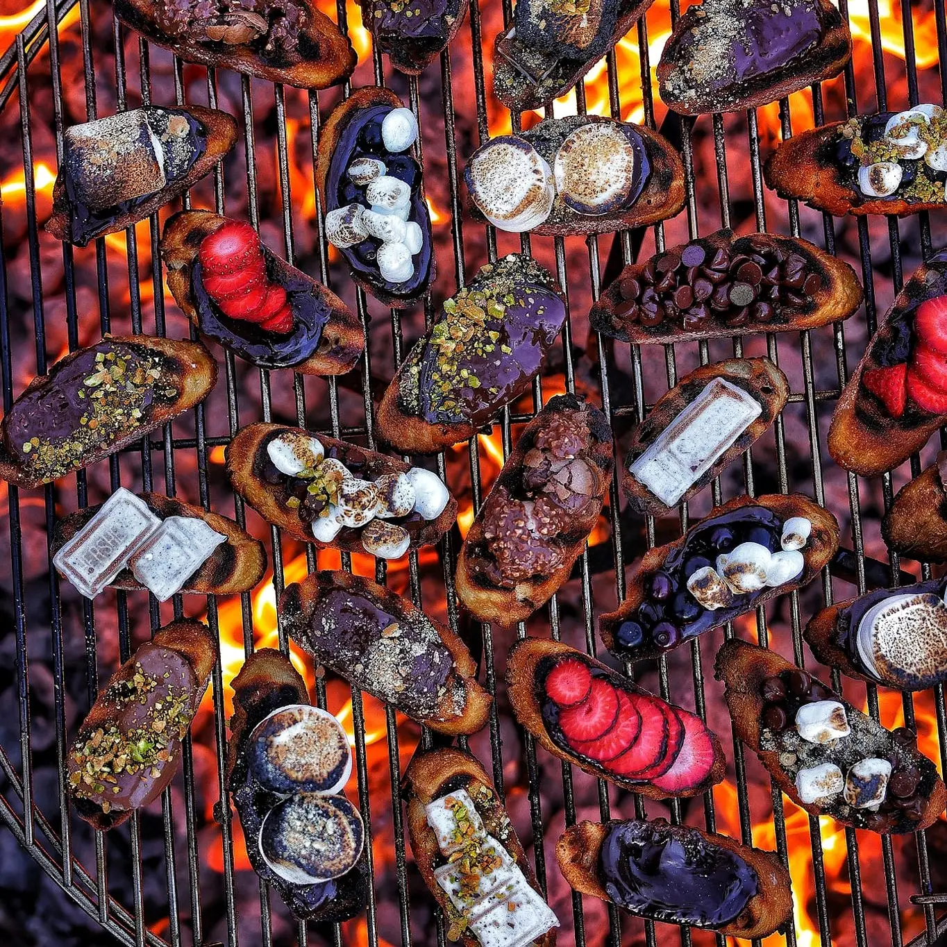Grilled dessert bread topped with chocolate, fruit, marshmallows, and nuts over open flames.