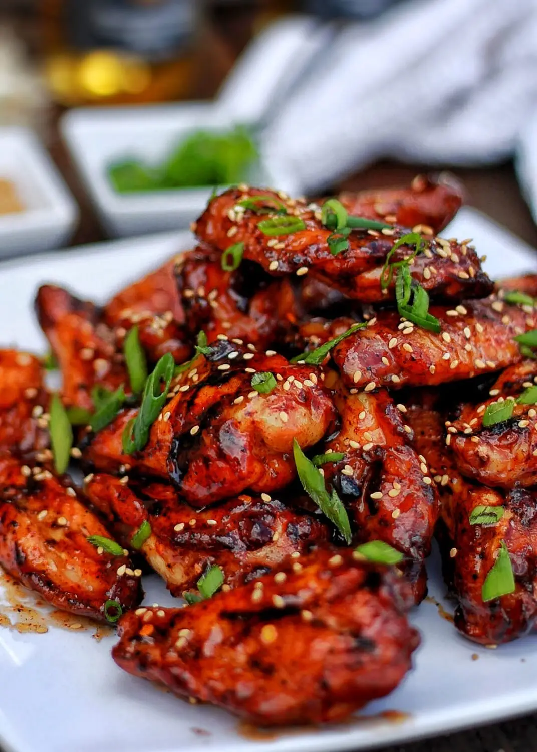 Grilled chicken wings garnished with sesame seeds and green onions on a white plate. Delicious BBQ appetizer.