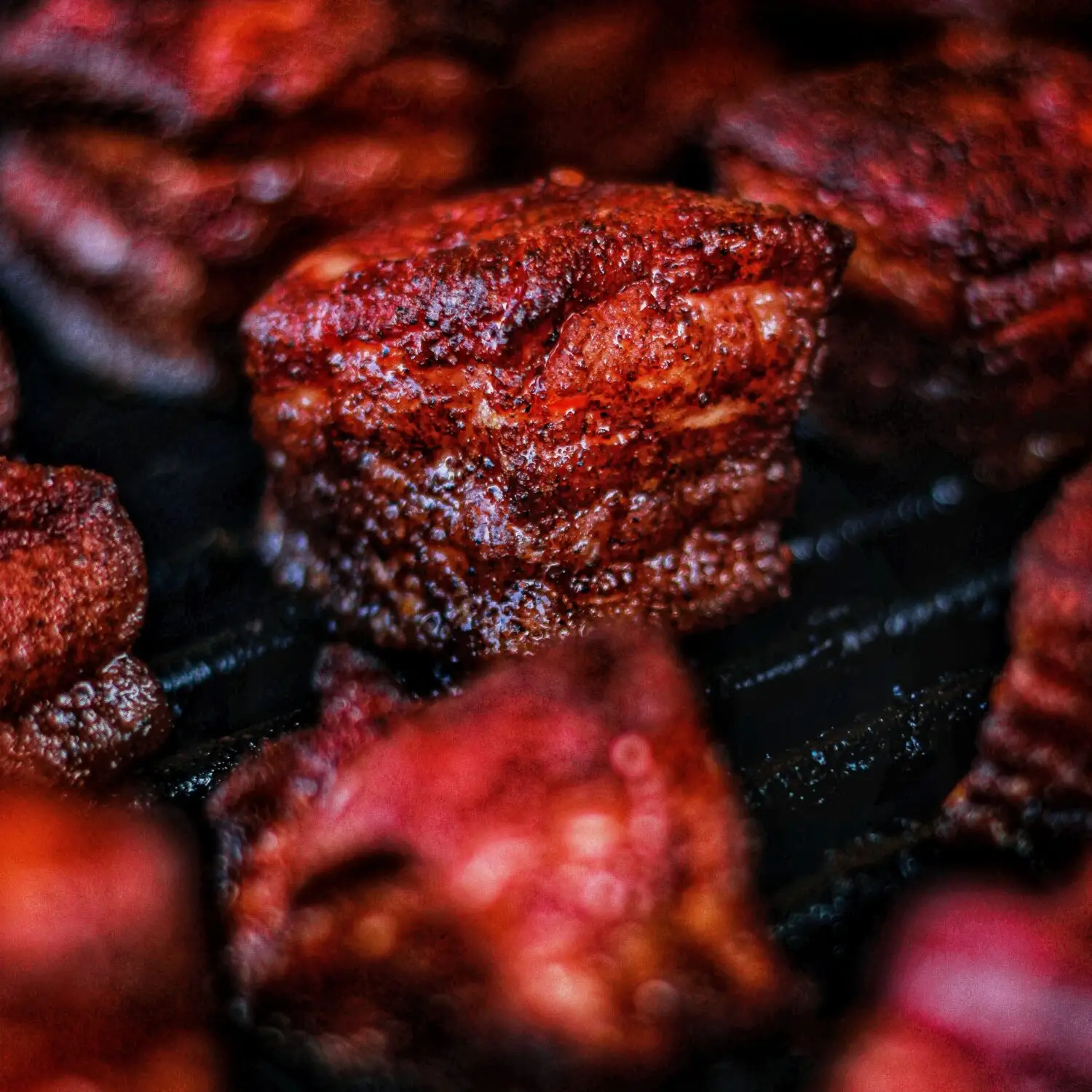 Close-up of juicy, smoked pork burnt ends on a grill, showcasing a rich, savory glaze and perfectly charred texture.