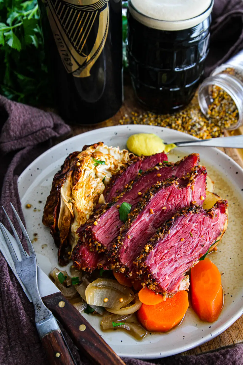 Sliced corned beef with cabbage, carrots, and mustard, paired with a dark beer on a rustic table setting.