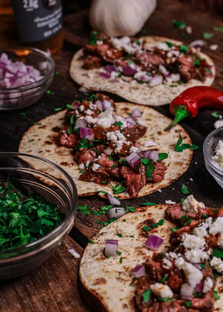 Delicious steak tacos with diced onions and fresh cilantro on a wooden table, garnished with cheese.