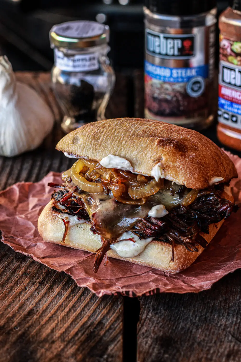 Gourmet brisket sandwich with caramelized onions on rustic wood table, seasoned with spices, and garlic.