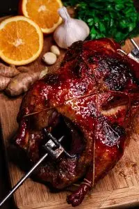 Roasted duck with crispy skin on a wooden board, surrounded by fresh orange, garlic, and parsley. Perfect for gourmet meals.