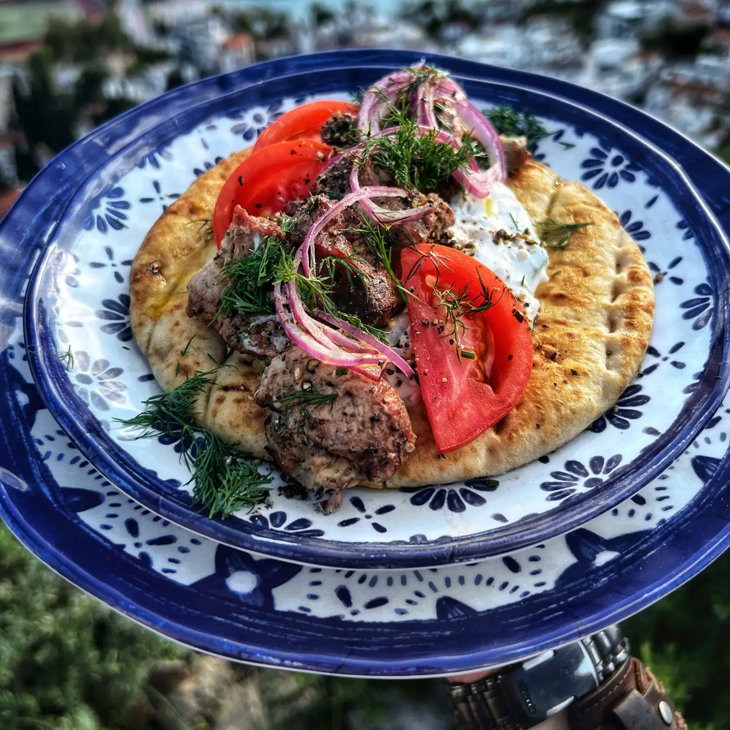 Delicious Greek souvlaki with tomatoes, onions, and dill on pita, served on a decorative blue and white plate.
