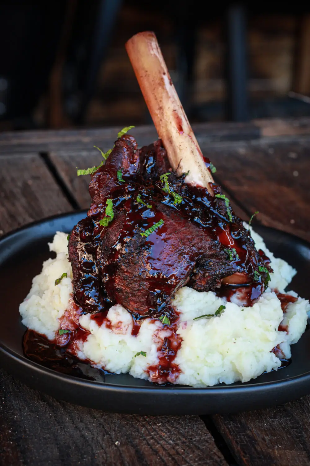 Gourmet lamb shank with rich glaze over creamy mashed potatoes on a rustic wooden table setting.