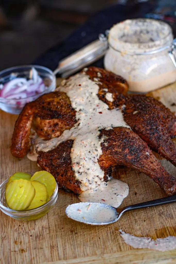 Grilled chicken with creamy sauce on a wooden board, served with pickles and onions.