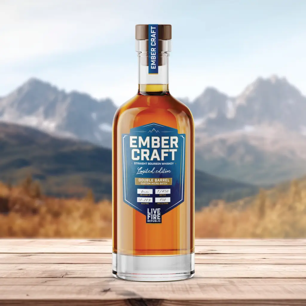 Bottle of Ember Craft bourbon on a wooden table with a mountain landscape in the background.