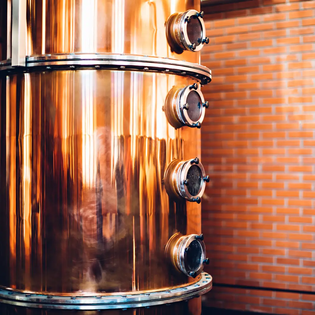 Copper distillation column in a distillery with brick wall background.