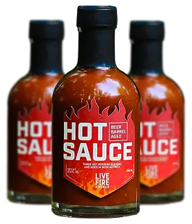Three bottles of beer barrel-aged hot sauce with fiery red labels featuring flames and bold text.