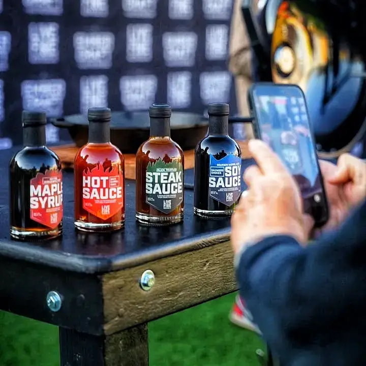 Person photographing four condiment bottles on a wooden table